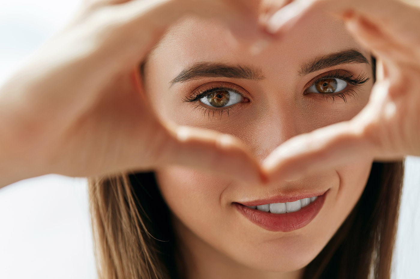 Nahaufnahme einer Frau mit Händen, die ein Herz um ihre Augen formen - Entscheidungshilfe Wimpernlifting oder Wimpernverlängerung